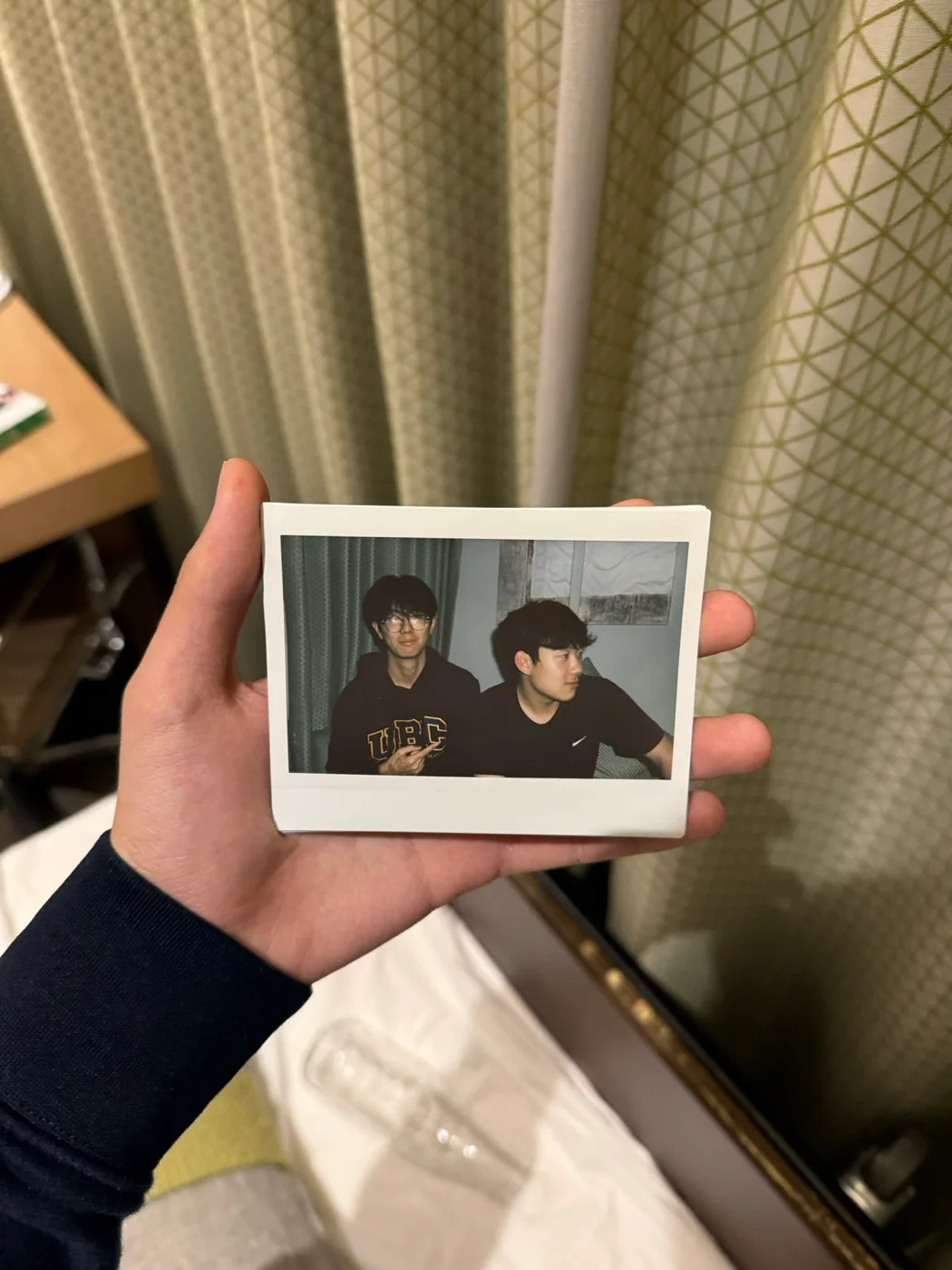 A hand holding a small printed photograph of two friends