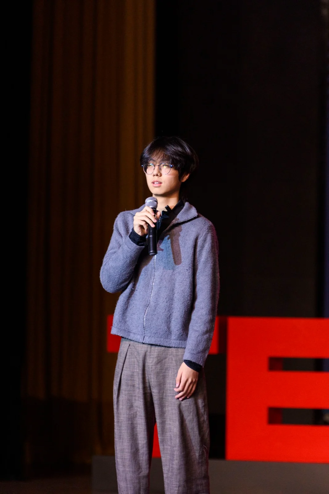 A full-length photograph of Rayn Lee speaking on stage at TEDxOTIA Youth
